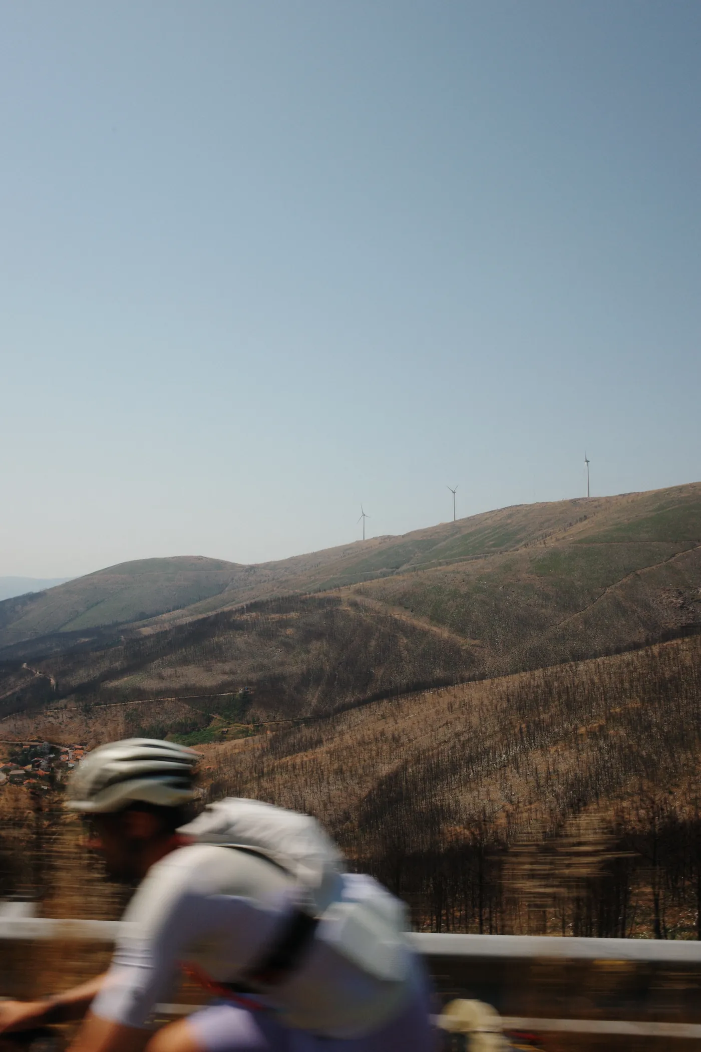 A motion-blurred cyclist passing a ridgeline lined with wind turbines