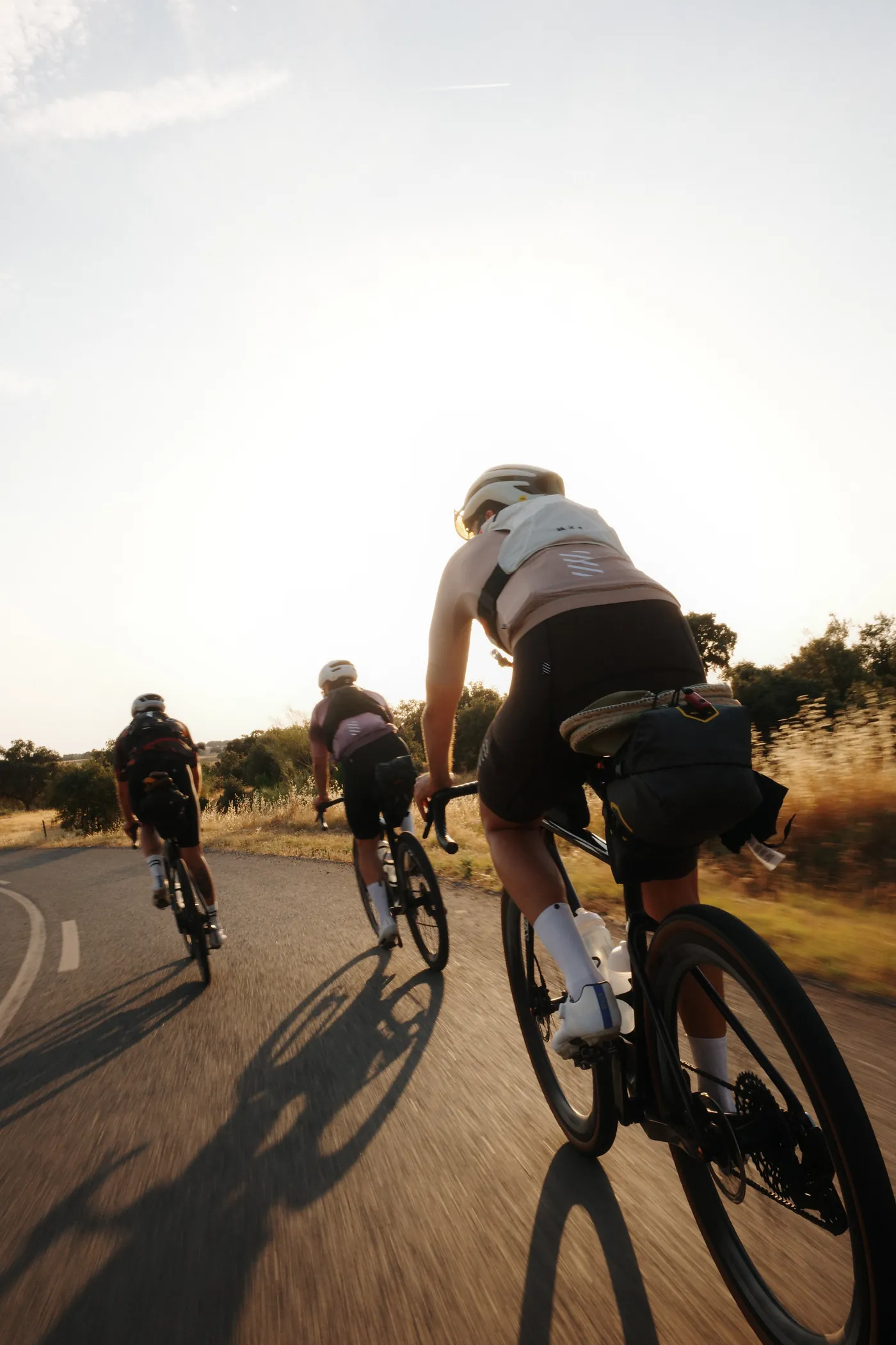 Three cyclists riding a back road at golden hour, seen from behind