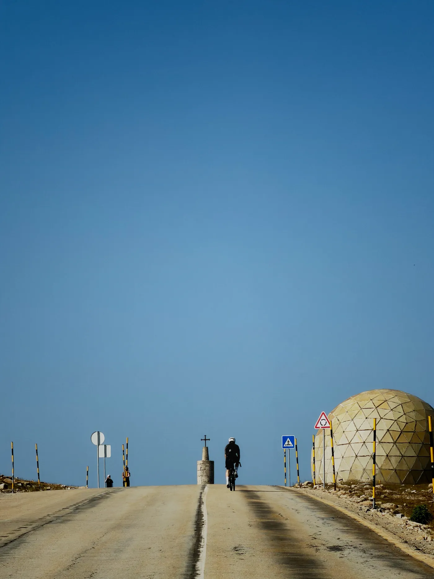 A cyclist rides toward the summit of Torre in the Serra da Estrela, beside its golden geodesic radar dome