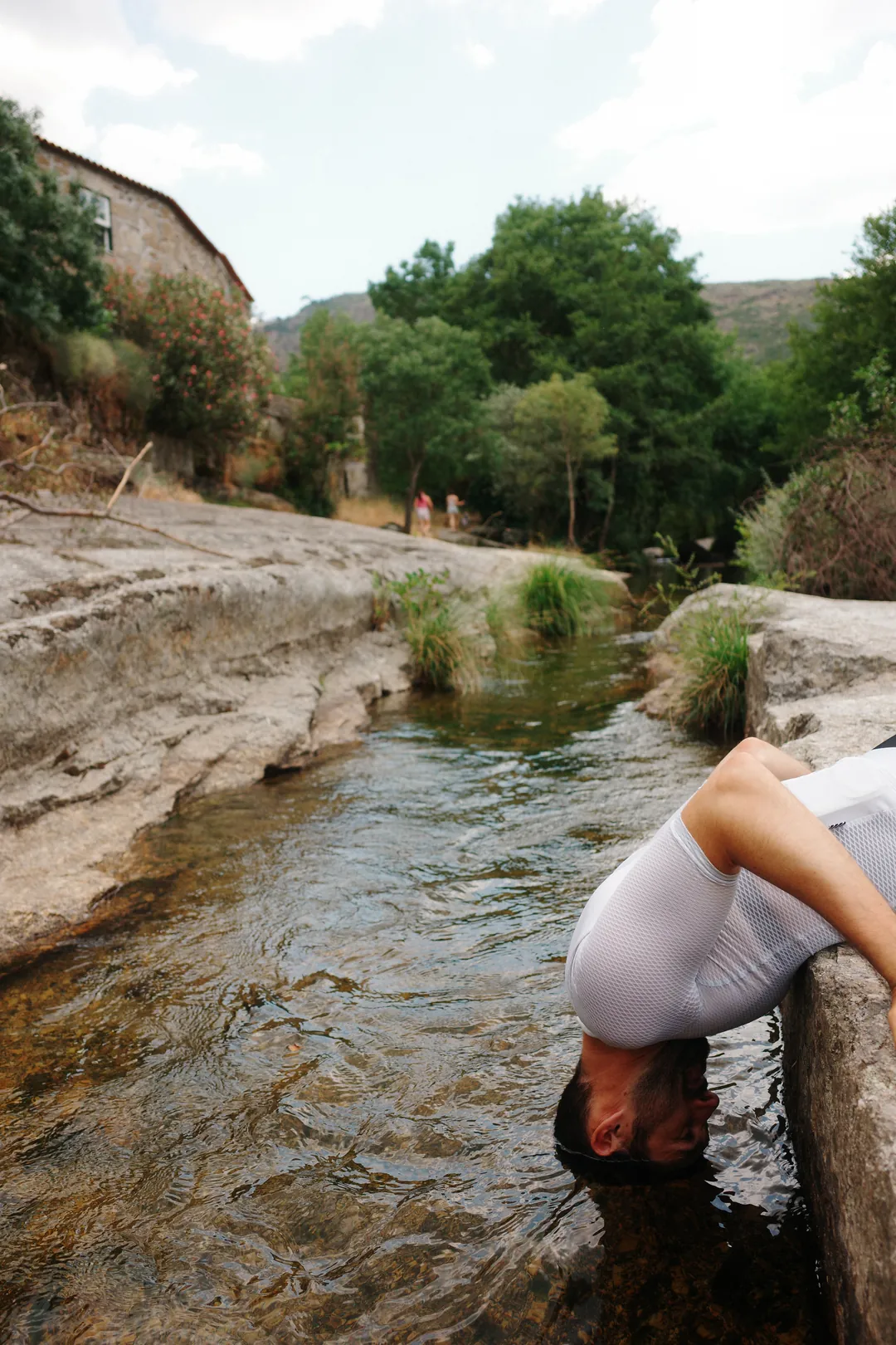 A cyclist lying back on a rock with his head submerged in a shallow stream