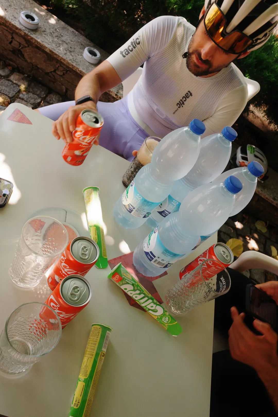 A café table at a ride stop covered with large bottles of water, cans of Coke, glasses and ice lollies